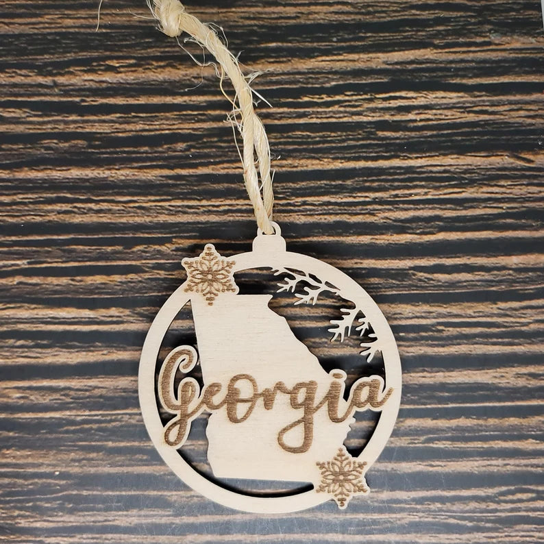 An Insanely Paracord Georgia State Christmas Ornament - Laser Engraved Birch Wood featuring the state's outline with "Georgia" in cursive. This charming piece of holiday décor is adorned with two snowflakes and rustic twine for hanging, set against a dark wood background.