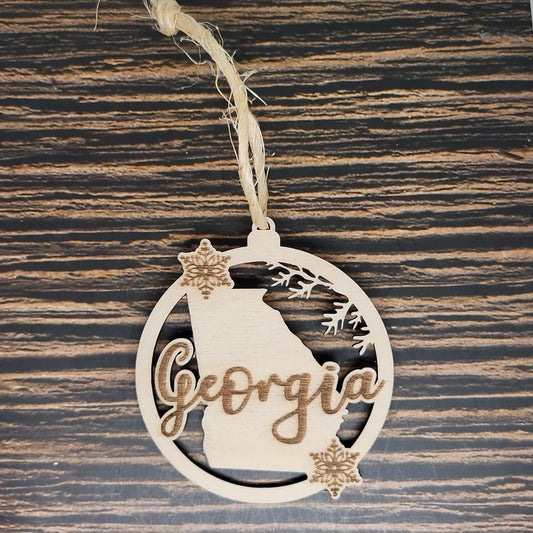 An Insanely Paracord Georgia State Christmas Ornament - Laser Engraved Birch Wood featuring the state's outline with "Georgia" in cursive. This charming piece of holiday décor is adorned with two snowflakes and rustic twine for hanging, set against a dark wood background.