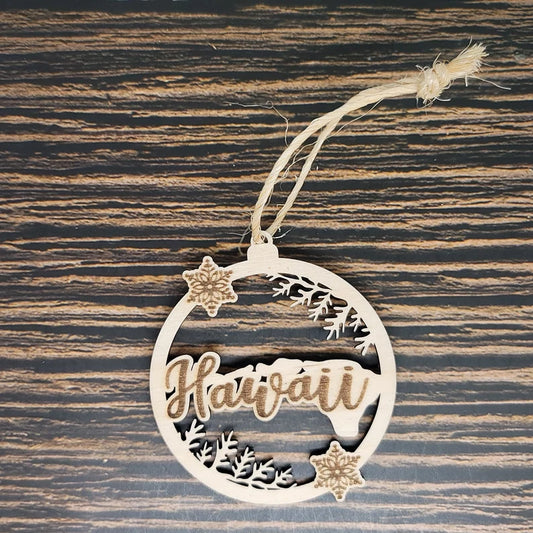 A round birch wood ornament with the word "Hawaii" intricately laser engraved in the center. The design includes small floral shapes and patterns around the circle. A piece of twine is tied at the top for hanging. The background is a dark, striped wood surface. Perfect as an Insanely Paracord Hawaii Christmas Ornament - 3" Tall Laser Engraved Birch Wood.