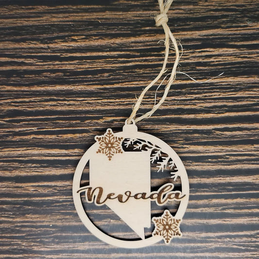 The Nevada State Laser Engraved Wood Christmas Ornament by Insanely Paracord features the word "Nevada" elegantly engraved in cursive. This circular piece features a detailed laser engraving of the Nevada state outline and two delicate snowflakes. Attached to a string for easy hanging, its textured wood background adds rustic charm.