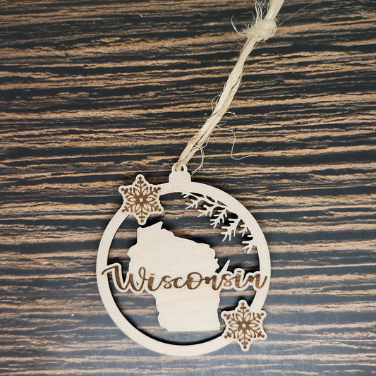 A Wisconsin State Christmas Ornament - Laser Engraved Birch Wood - 3" Tall, 2.75" Wide by Insanely Paracord featuring an outline of Wisconsin in the center with snowflakes above and below. The word "Wisconsin" is cut out in a script font across the state outline. This holiday decor piece hangs from a rustic twine loop, resting on a dark wood background.