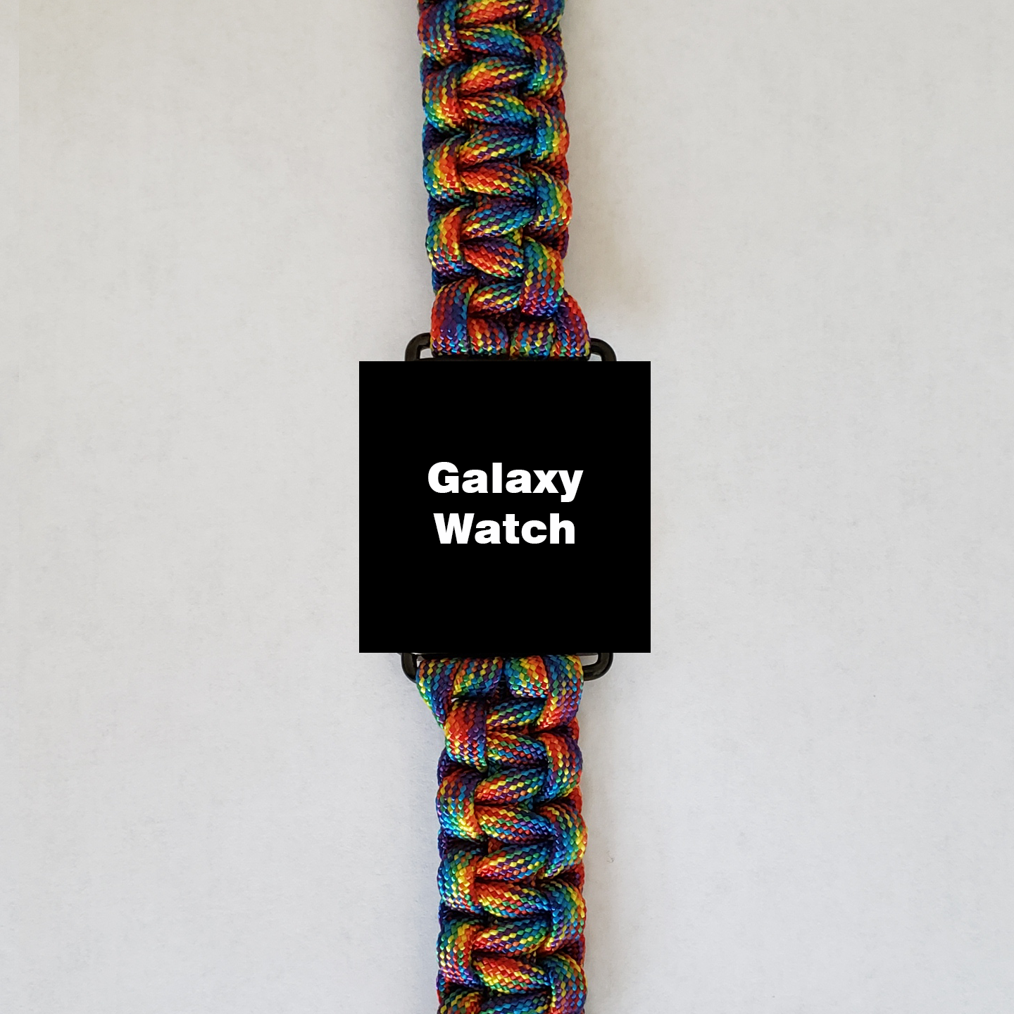 A smart watch with the text "Galaxy Watch" on its screen is shown against a plain background. The intricately woven watch band is an Insanely Paracord Galaxy Watch 42mm Paracord Watch Band - High-Quality, Durable, & Stylish, featuring vibrant, multicolored strands that catch the eye.