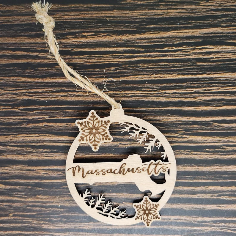 An Insanely Paracord Massachusetts State Christmas Ornament - Laser Engraved Birch Wood Twine Tie, laser engraved with "Massachusetts" in the center. It features two snowflakes and a silhouette of the state, with a rustic twine loop for hanging. The dark wood background showcases light, natural grain patterns, perfect holiday decor for your tree.