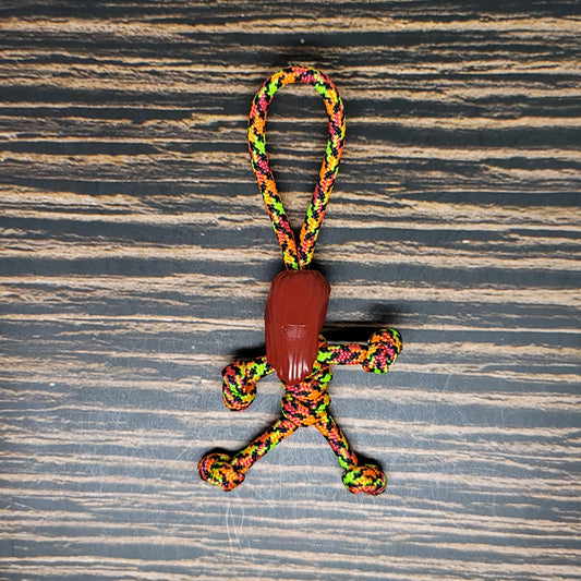 A colorful Nightmare Pumpkin Queen Keychain | Handmade Paracord Pal, shaped like a stick figure person with a brown wooden bead as the head, lies on a striped wooden surface. This handmade Halloween accessory from Insanely Paracord features vibrant colors including green, yellow, orange, and pink, making it a festive and unique addition to any collection.